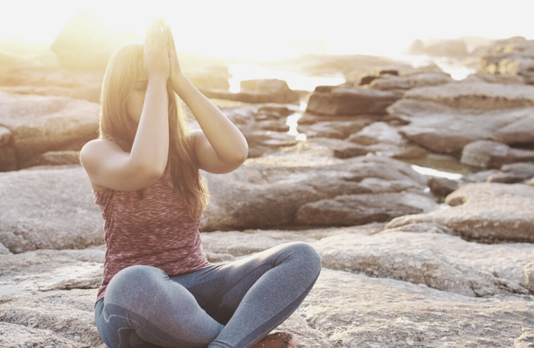 Was hilft gegen Stress - Frau entspannt am Strand mit Yogapose